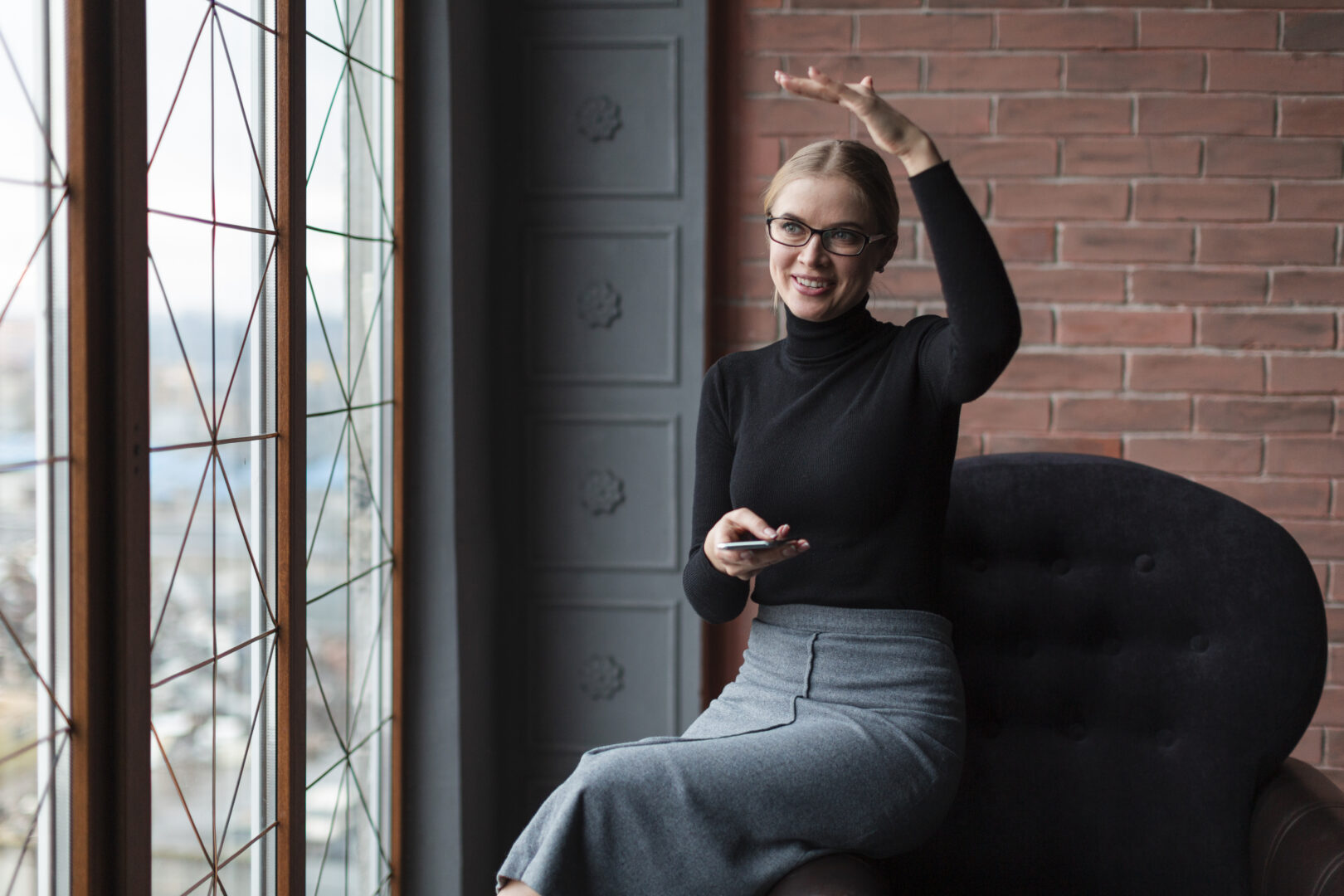 Smiling model in a black turtleneck and gray skirt posing confidently indoors, showing professionalism and positive energy on set.